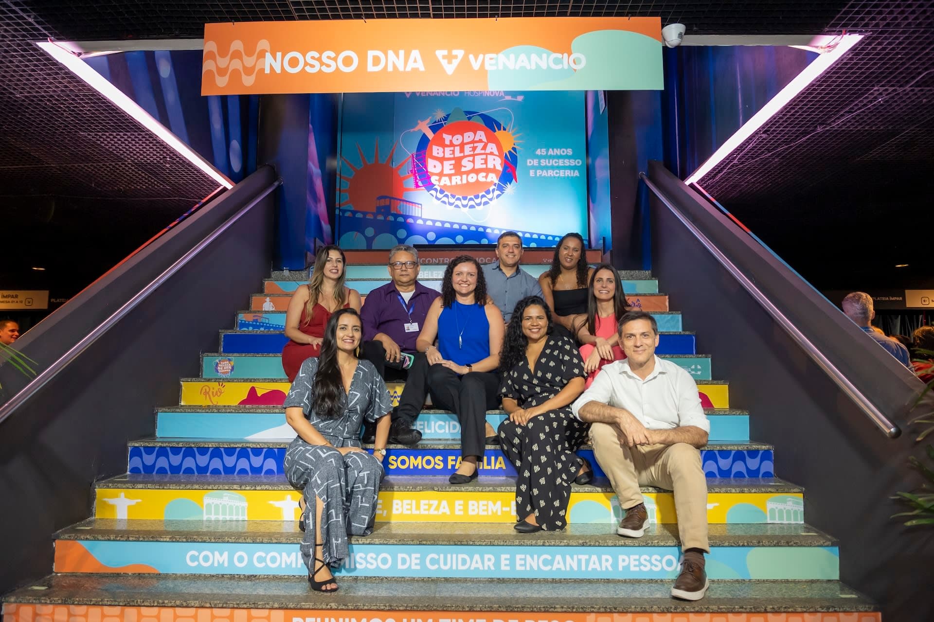 Grupo de convidados em escadaria colorida com tema "Toda beleza de ser carioca"