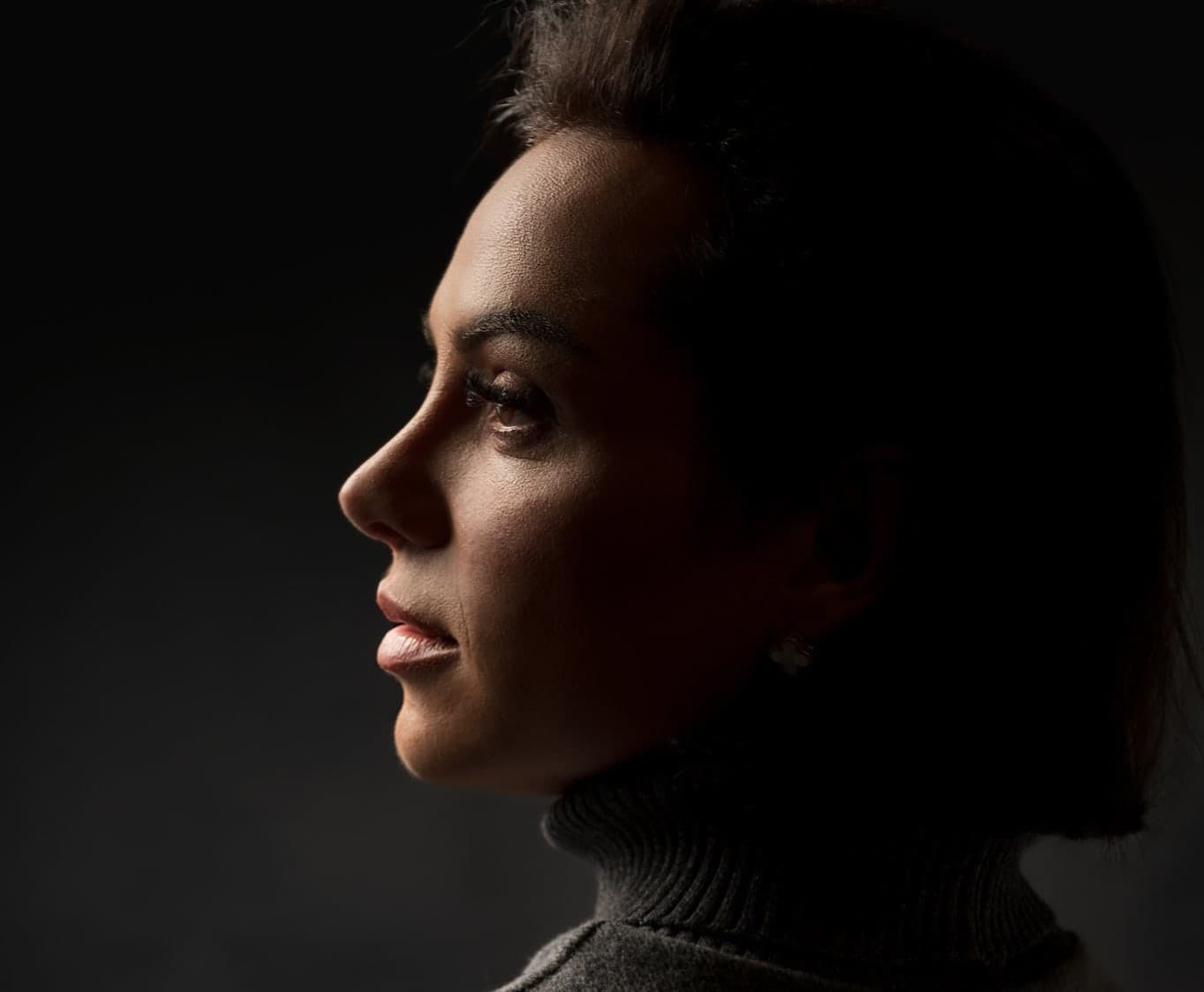 Retrato artístico em perfil com iluminação dramática transmitindo introspeccão e elegância profissional contra fundo preto