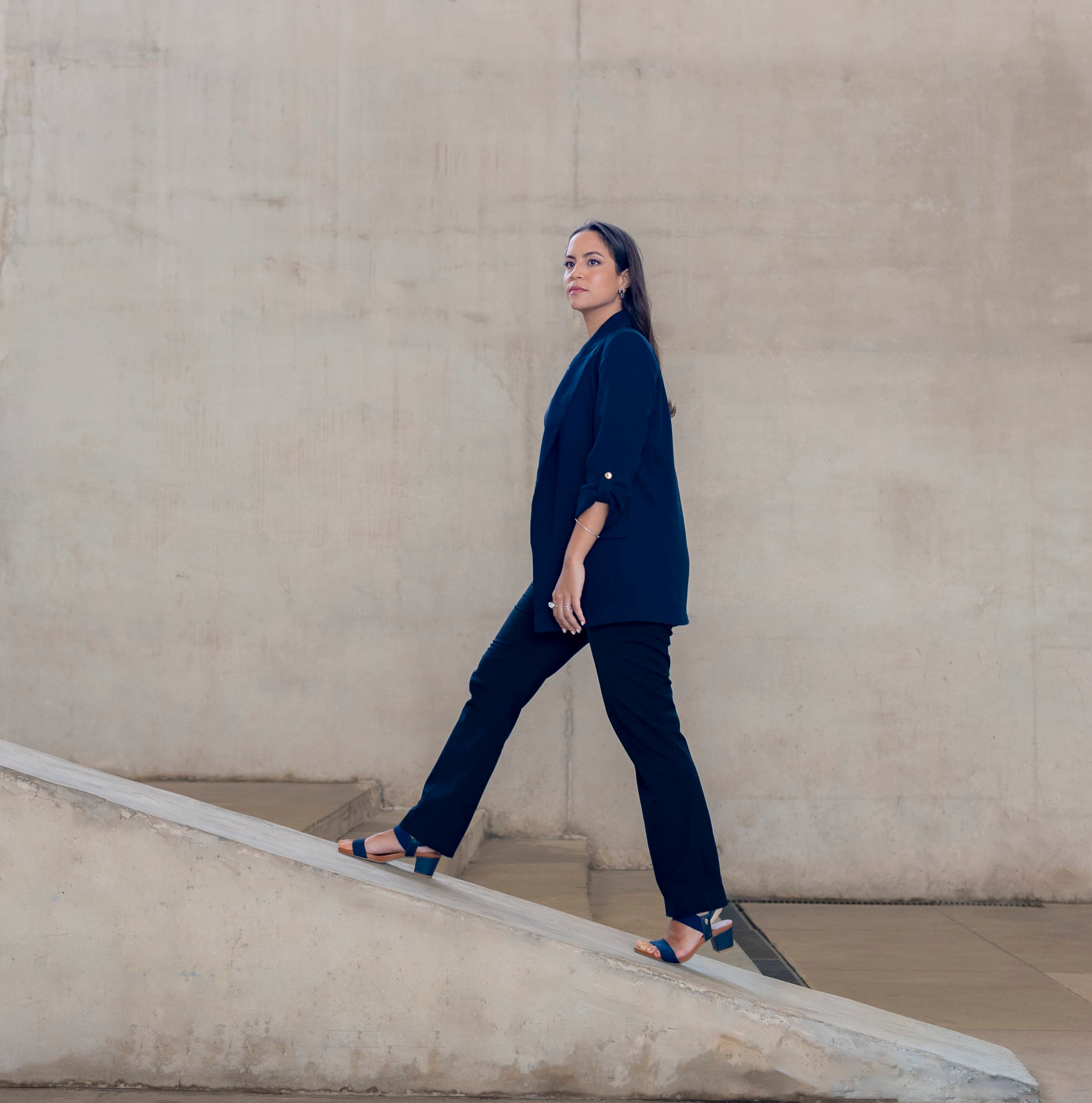 Mulher em pose segura usando blazer executivo preto em retrato profissional contra parede minimalista na Barra da Tijuca, Rio de Janeiro