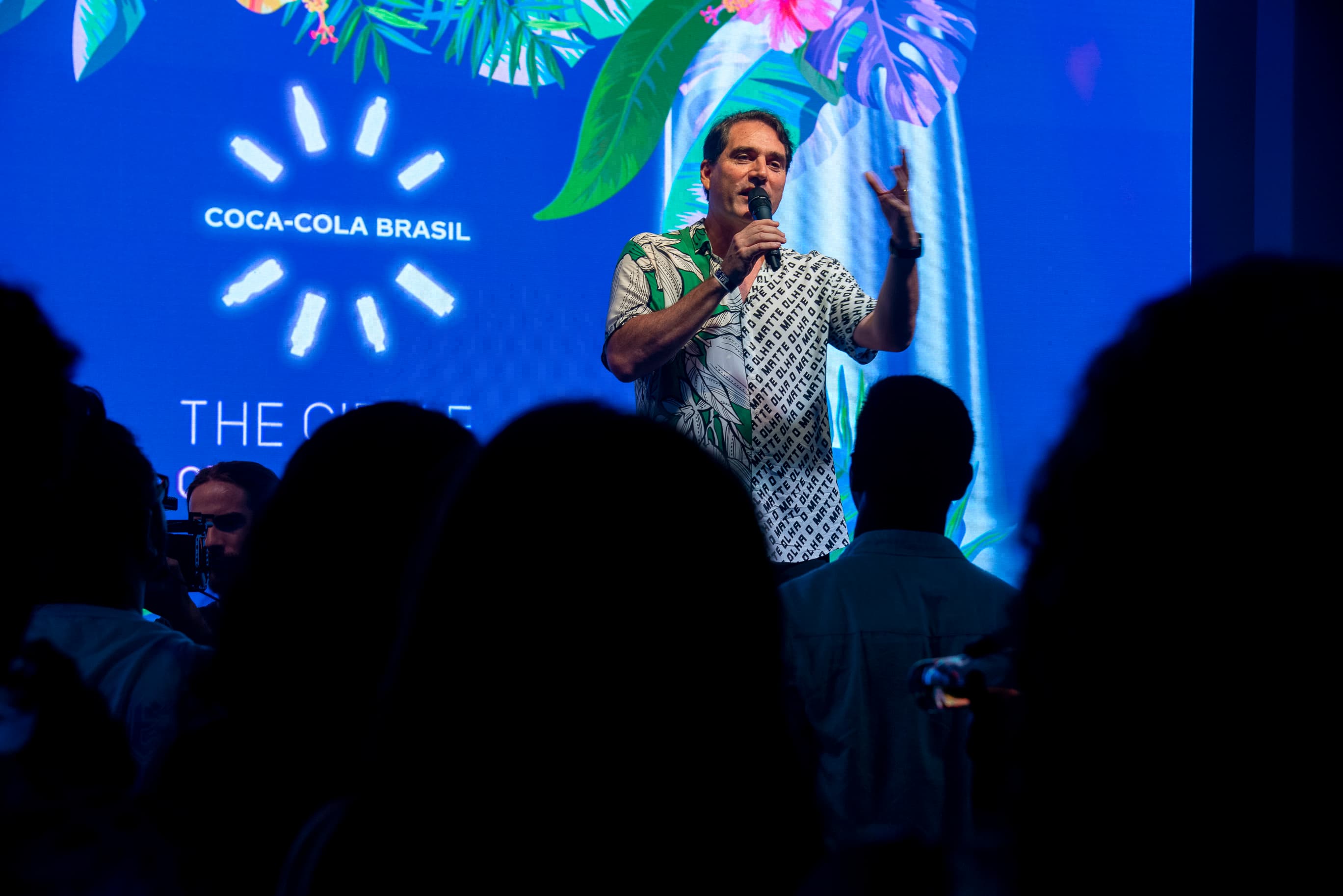 Palestrante de camisa havaiana discursando no palco do evento "The Circle" da Coca-Cola Brasil